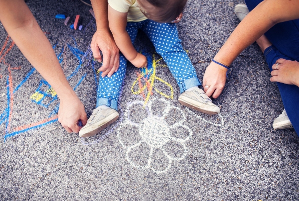 close-up-of-little-girl-and-her-parents-drawing-with-chalks-on-the-sidewalk